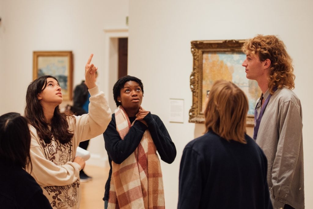 young people inside a gallery setting point out and look at an artwork that is out of frame