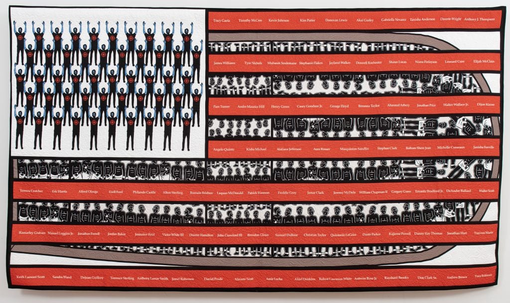 Carolyn Mazloomi, Hands Up ... Dont Shoot #2. A black, white, and red art quilt in the form of an American flag. The red stripes, printed with the names of African Americans who died due to police violence, are super imposed over the form of ship transporting enslaved Africans across the ocean to live in bondage. The stars have been replaced with the figure of an African American man standing with his hands up, a bullseye on his chest. 