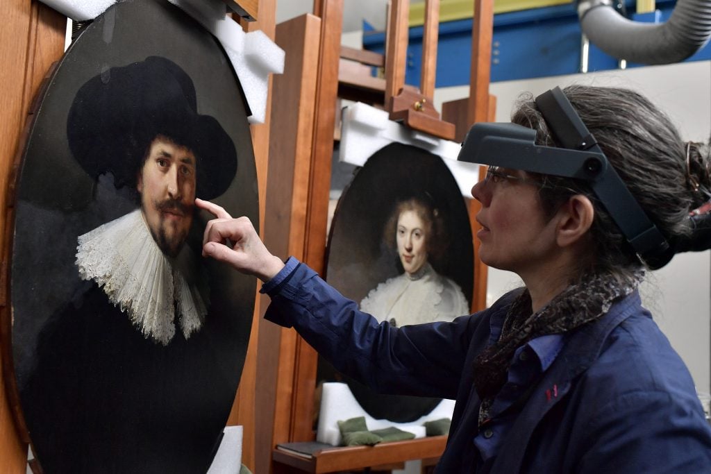 A woman wearing technical bifocals points at an old master painting she's restoring