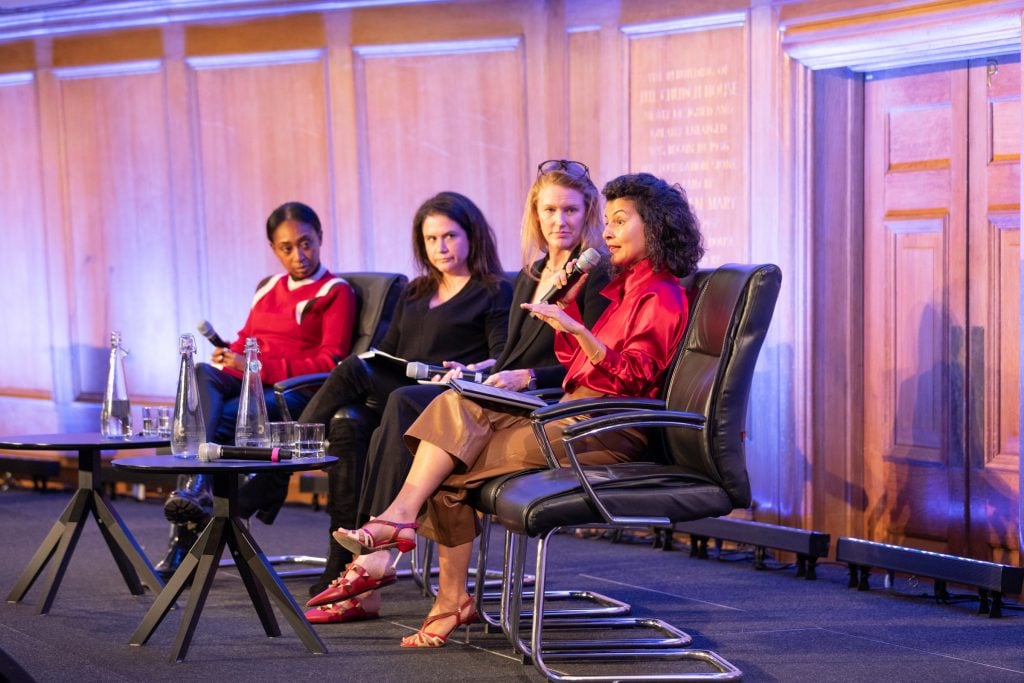 a photo of 4 women sitting on a stage speaking into microphones