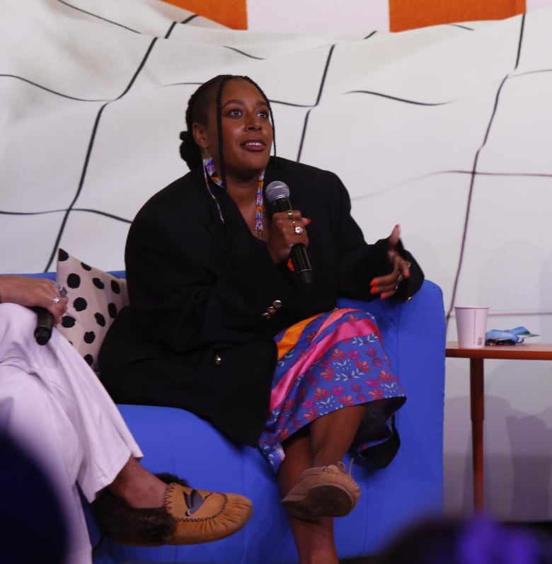 A woman in a ribbon skirt and moccasins speaking. 