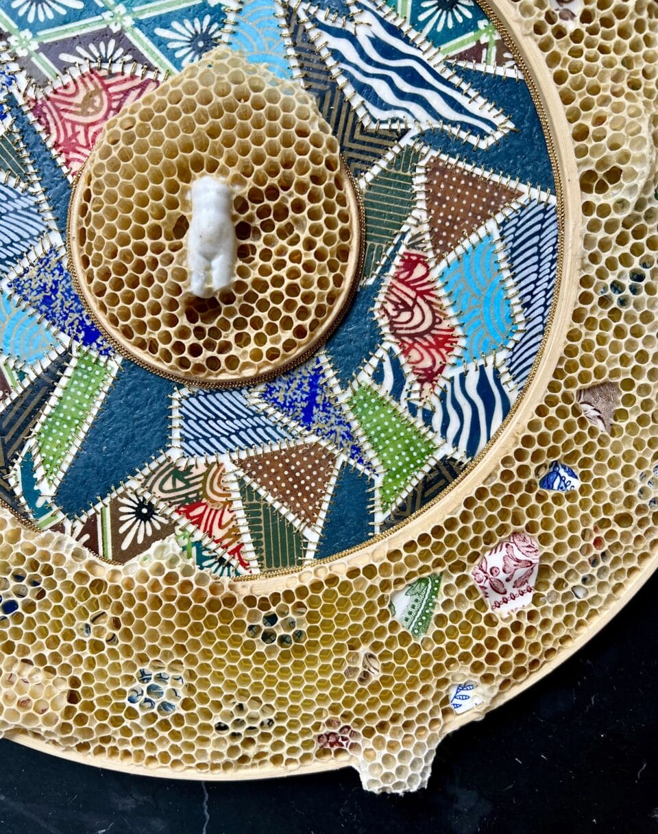 a detail image of embroidered patchwork with pottery shards stuck in honeycomb and a figurative sculpture at the center