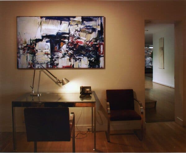 A painting on a wall above a modernist desk with a lamp and a telephone.