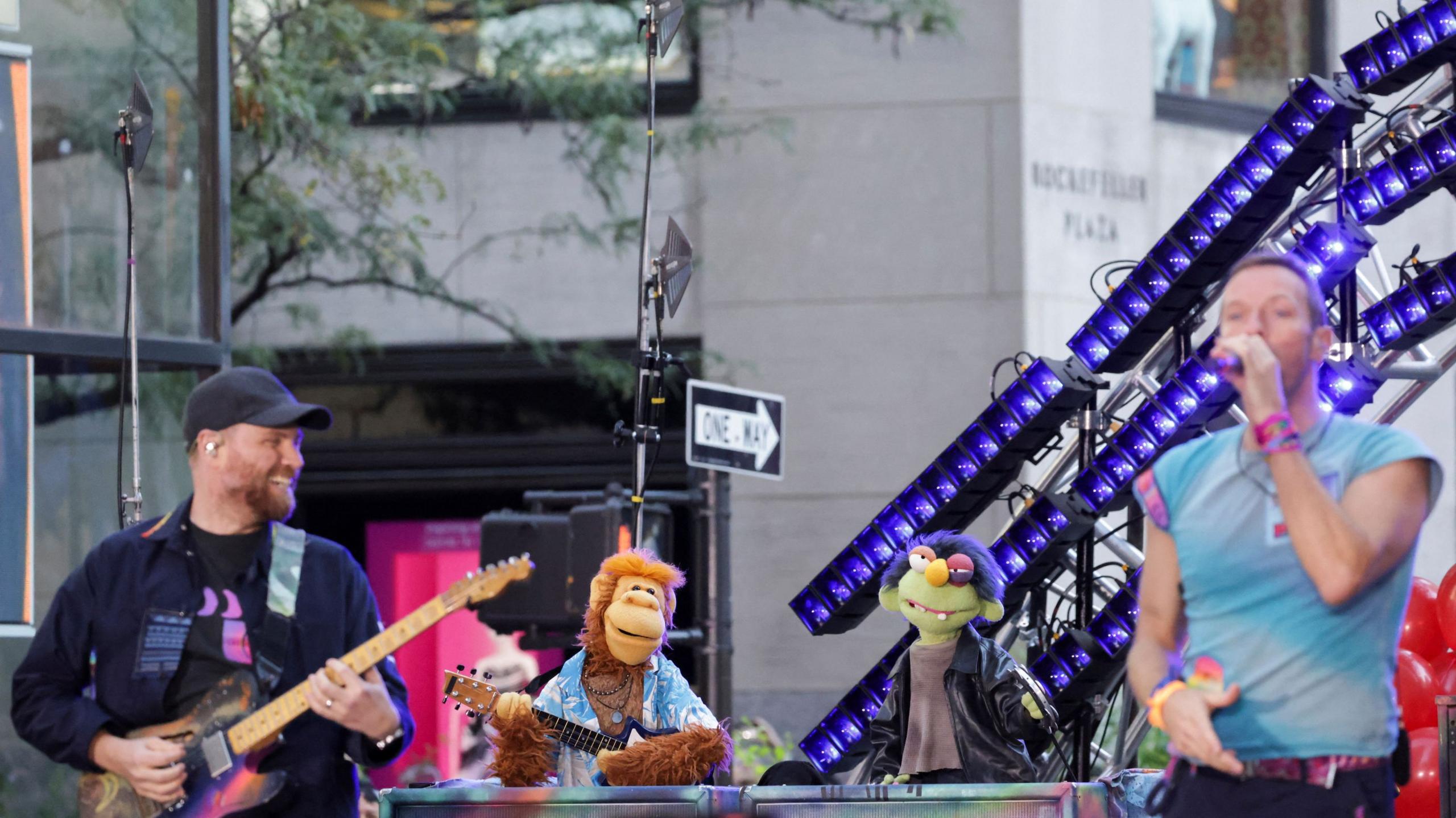 Coldplay and a bunch of muppets performing on stage on an American street