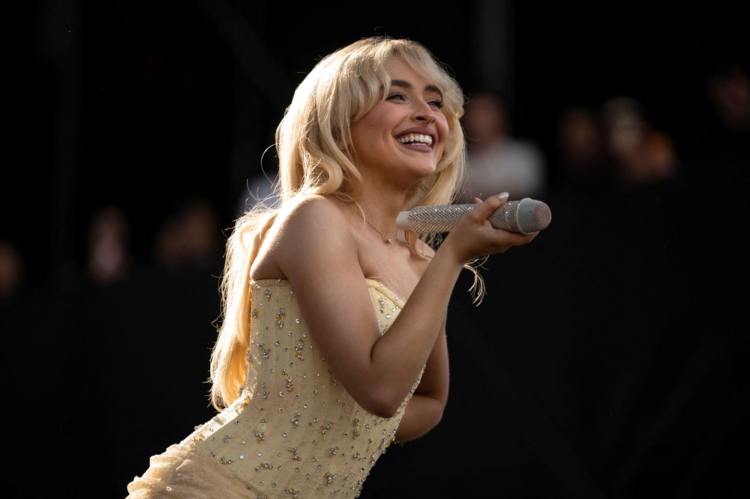 Sabrina Carpenter smiling while holding a microphone on stage