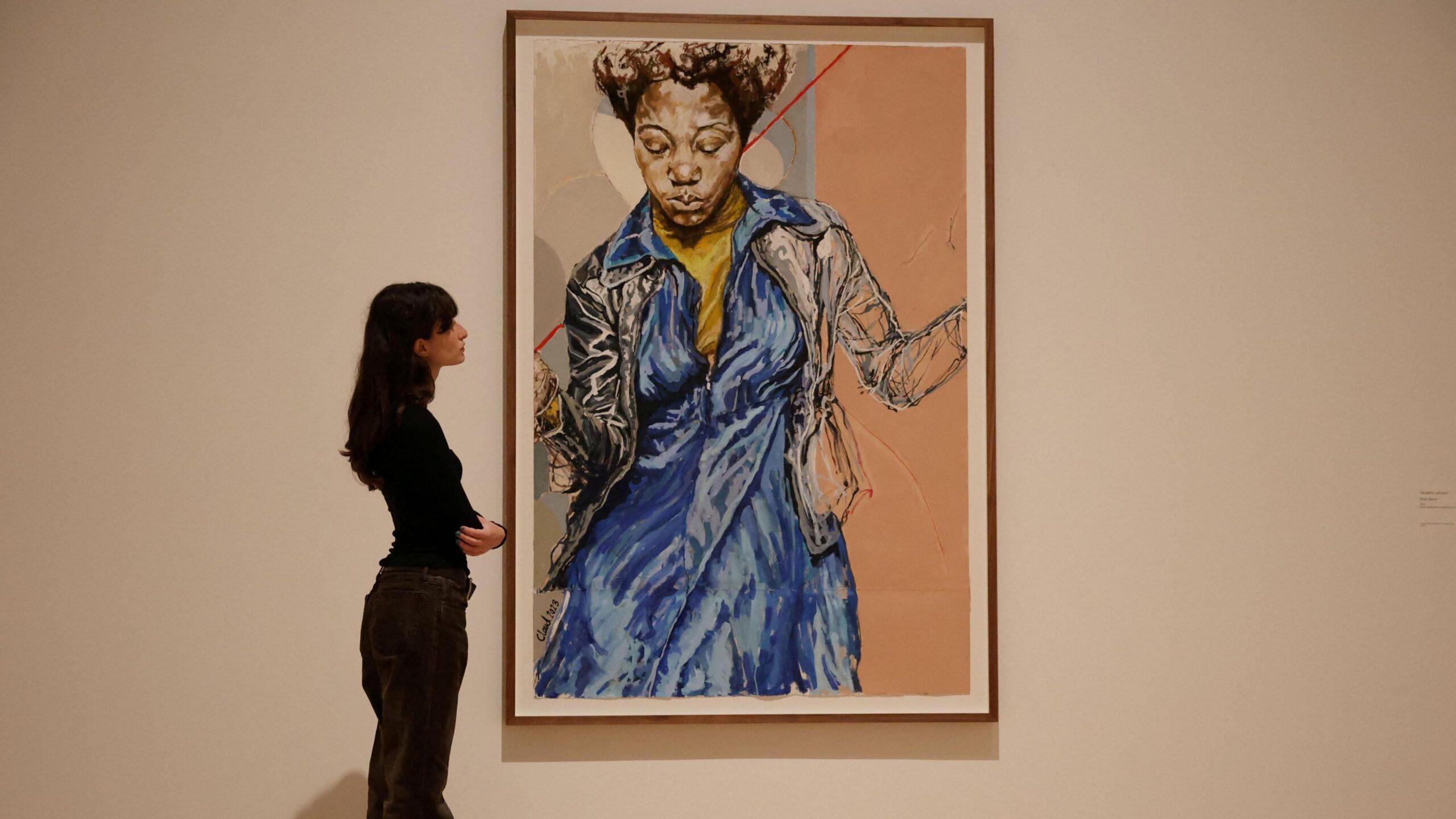 Gallery assistant posing alongside a Claudette Johnson portrait of a black woman in a blue dress at Tate Britain