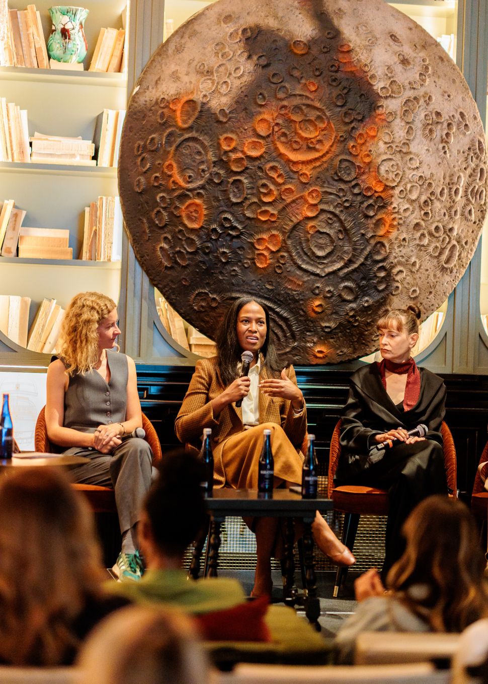 A trio of women sit on a couch on a dais to lead a panel discussion