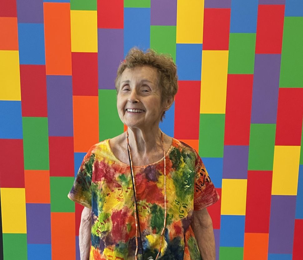 A woman in a bright tunic stands in front of an even brighter multicolor wall