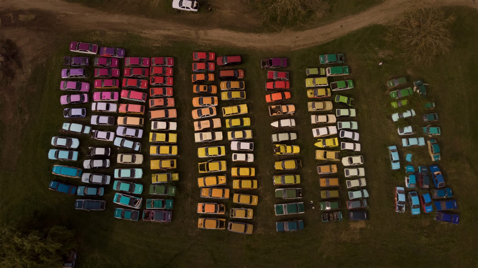 an aerial view of cars painted an arranged by color in a field