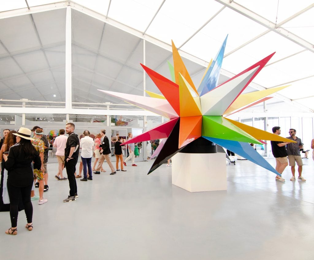 Installation view of Scope Art Show 2023 inside a cavernous white tent with a larg-scale sculpture comprised of huge stripes in different colors.