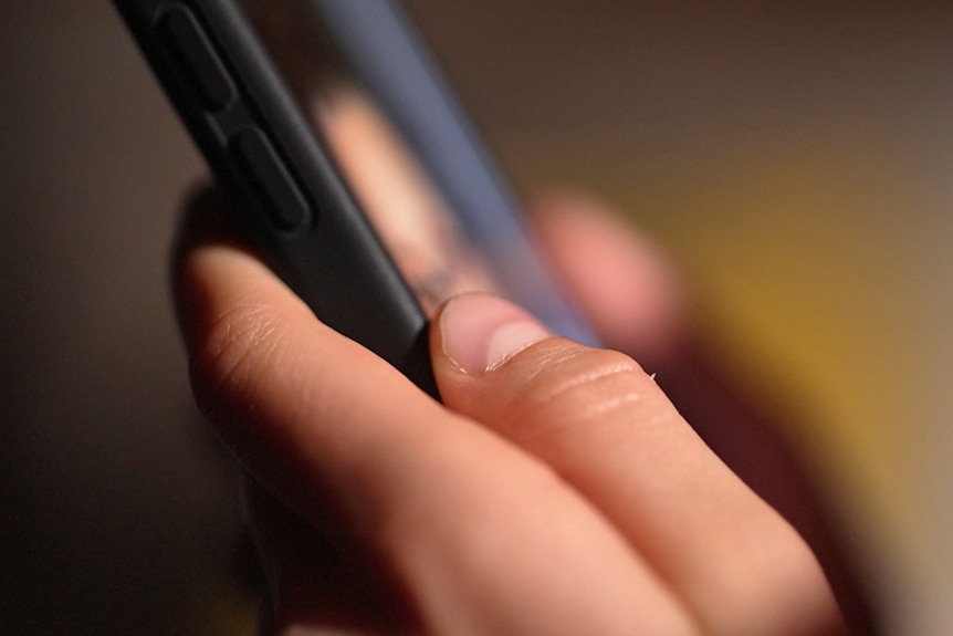Two hands hold a mobile phone in a slightly darkened room.