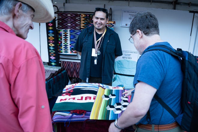 Fellow art collectors Marc Applebaum (left) and Ari Plosker shop for rugs at weaver Venancio Aragon's booth at the Santa Fe Indian Market on Aug. 17, 2024 in Santa Fe, New Mexico.