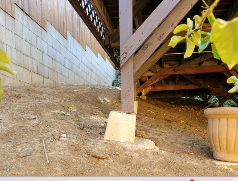 A wooden post of a desk of a home is precariously secured atop a concrete footing.