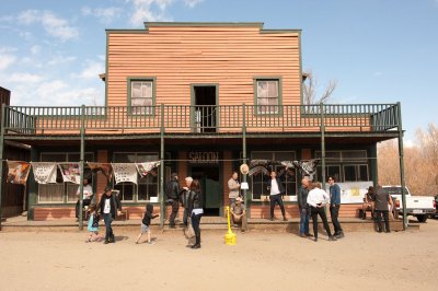 People walk by a two-story building in an old western town with the word 'Saloon' over the door. There is art there now. 