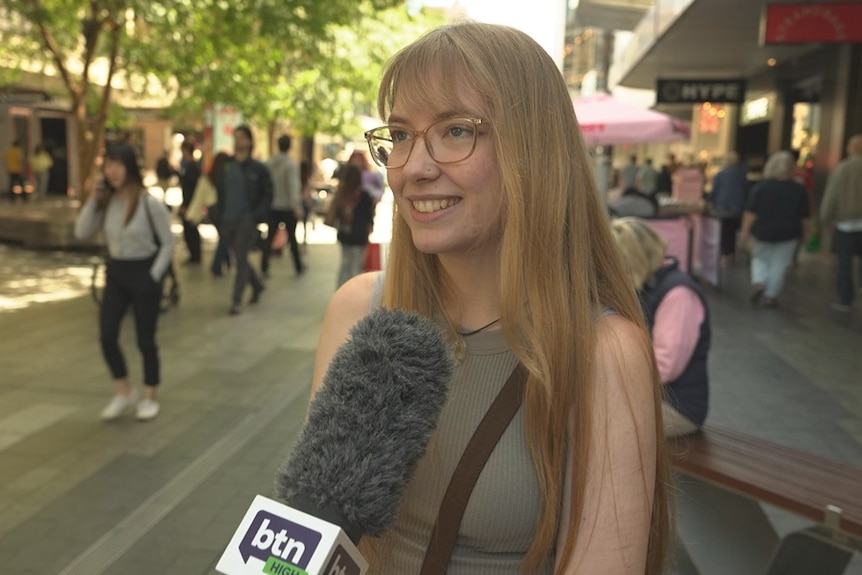 A young woman is interviewed in a busy mall.