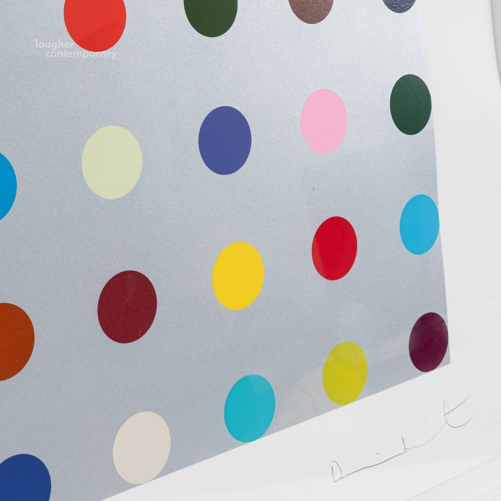 Close up detail of a print by Damien Hirst of a series of multicolor polka dots on a silver ground, with the artists signature in pencil at the bottom right, on offer by Lougher Contemporary.