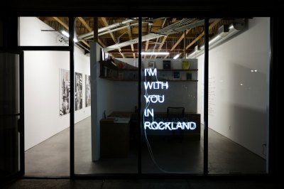 View of a gallery exterior at night showing a neon work that reads 'I'm With You in Rockland'. 