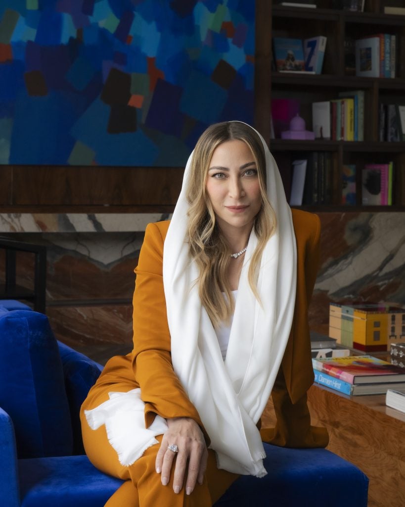 a woman in a white head scarf and yellow suit sits on a blue couch