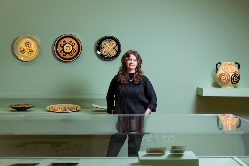 A woman with curly brown hair stands in a gallery full of cubism ceramics.