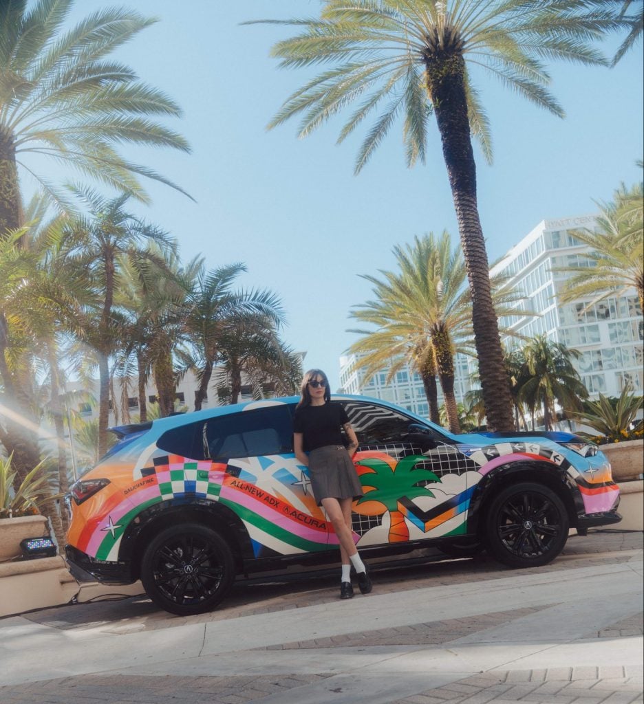 a woman in shorts leans against a colorful car 