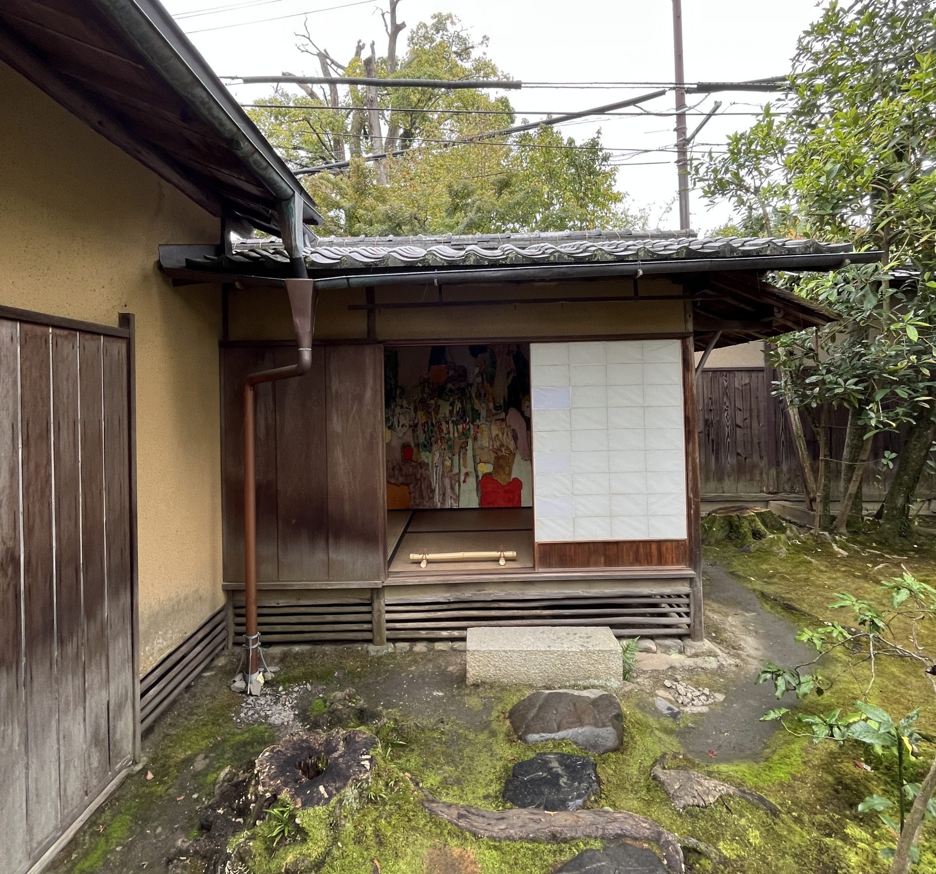 A small room with a door open to a sylvan garden holds an abstract painting.