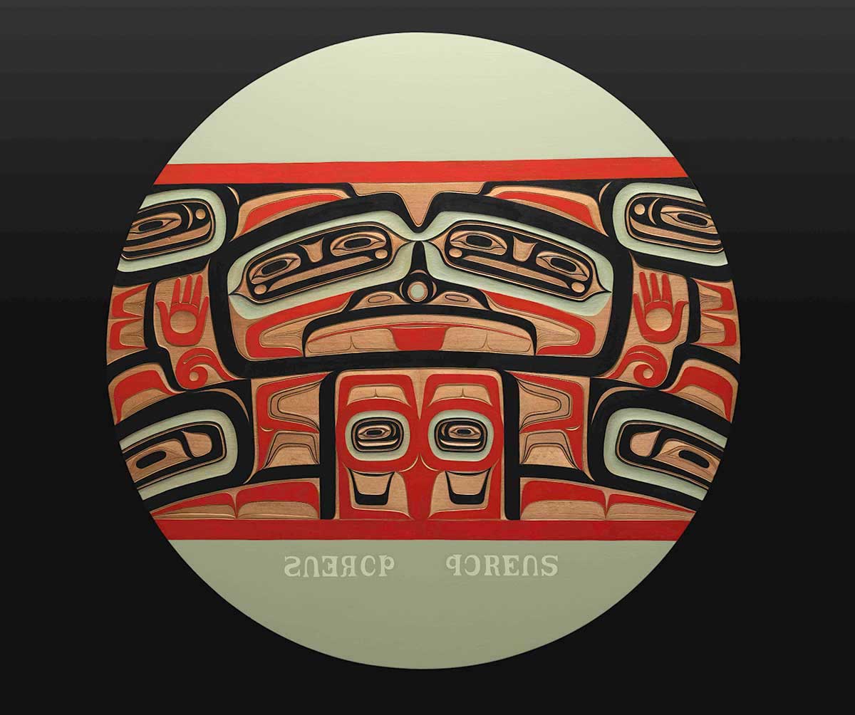 A circular piece of artwork in green holds a carving painted red, black and light green.