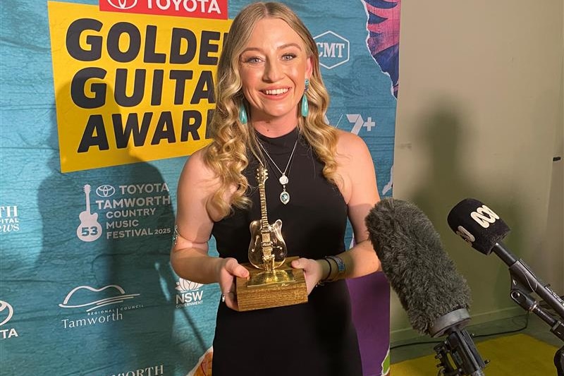 A woman smiles with a golden guitar trophy. 