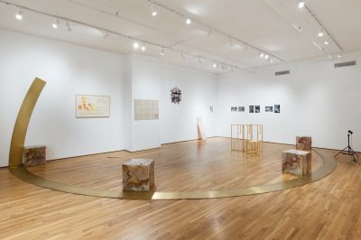 A gallery that has at its center three stone cubes with a golden arc surrounding them.