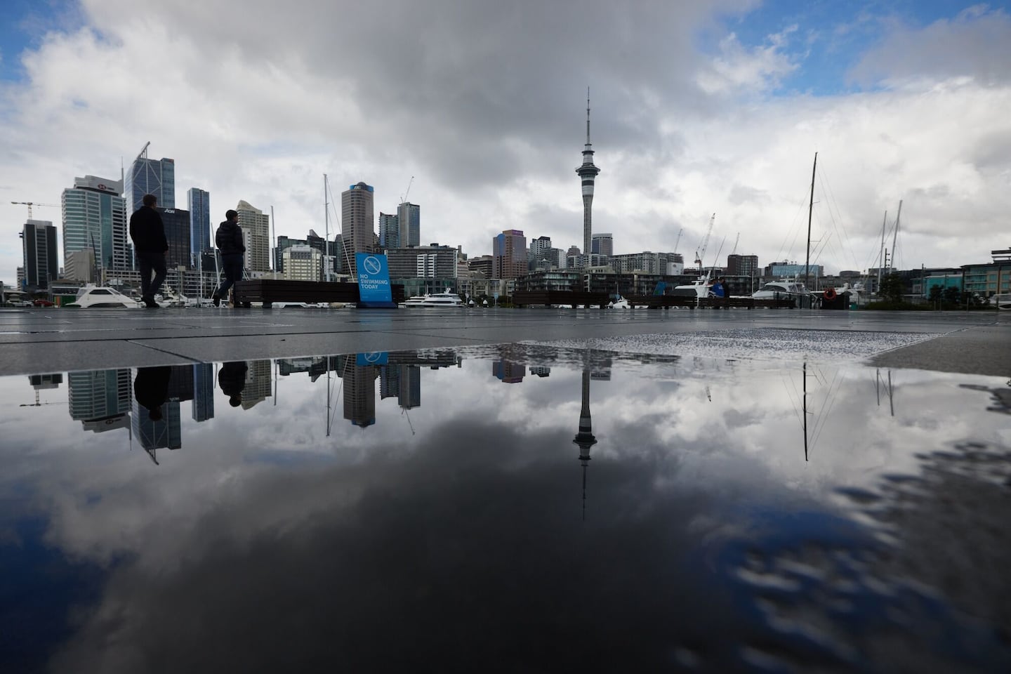 The Sky Tower, beyond pedestrians at a marina, in the central business district in Auckland, New Zealand.