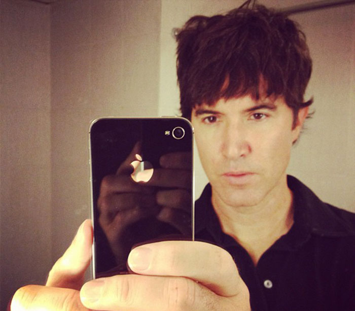 Person taking a selfie with a smartphone, wearing a black shirt; MySpace founder looks different.