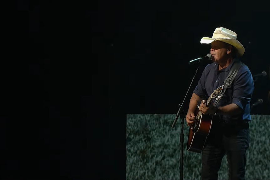 A man plays guitars and sings on stage. 