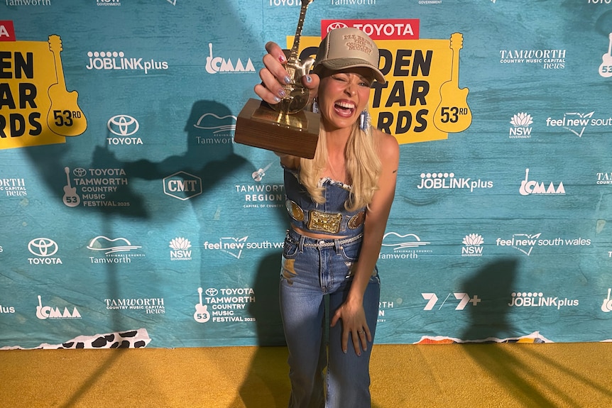 Max Jackson wearing double denim shows of her golden guitar trophy