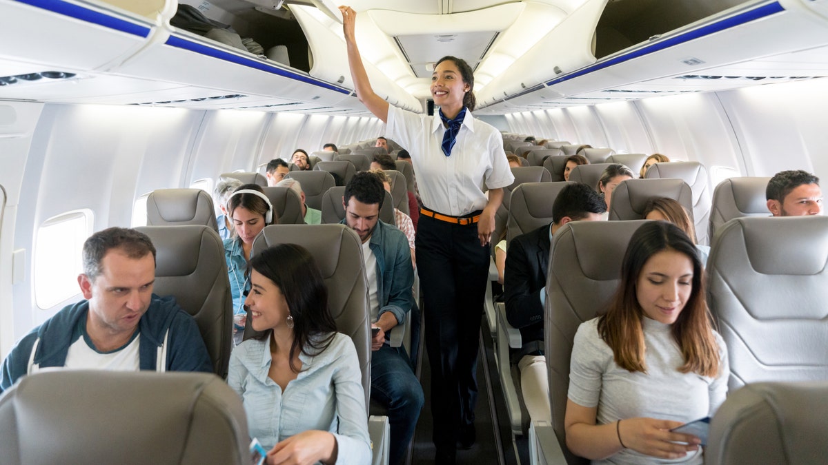 plane Happy flight attendant walking the aisle in an airplane closing overhead compartments and smiling - travel concepts