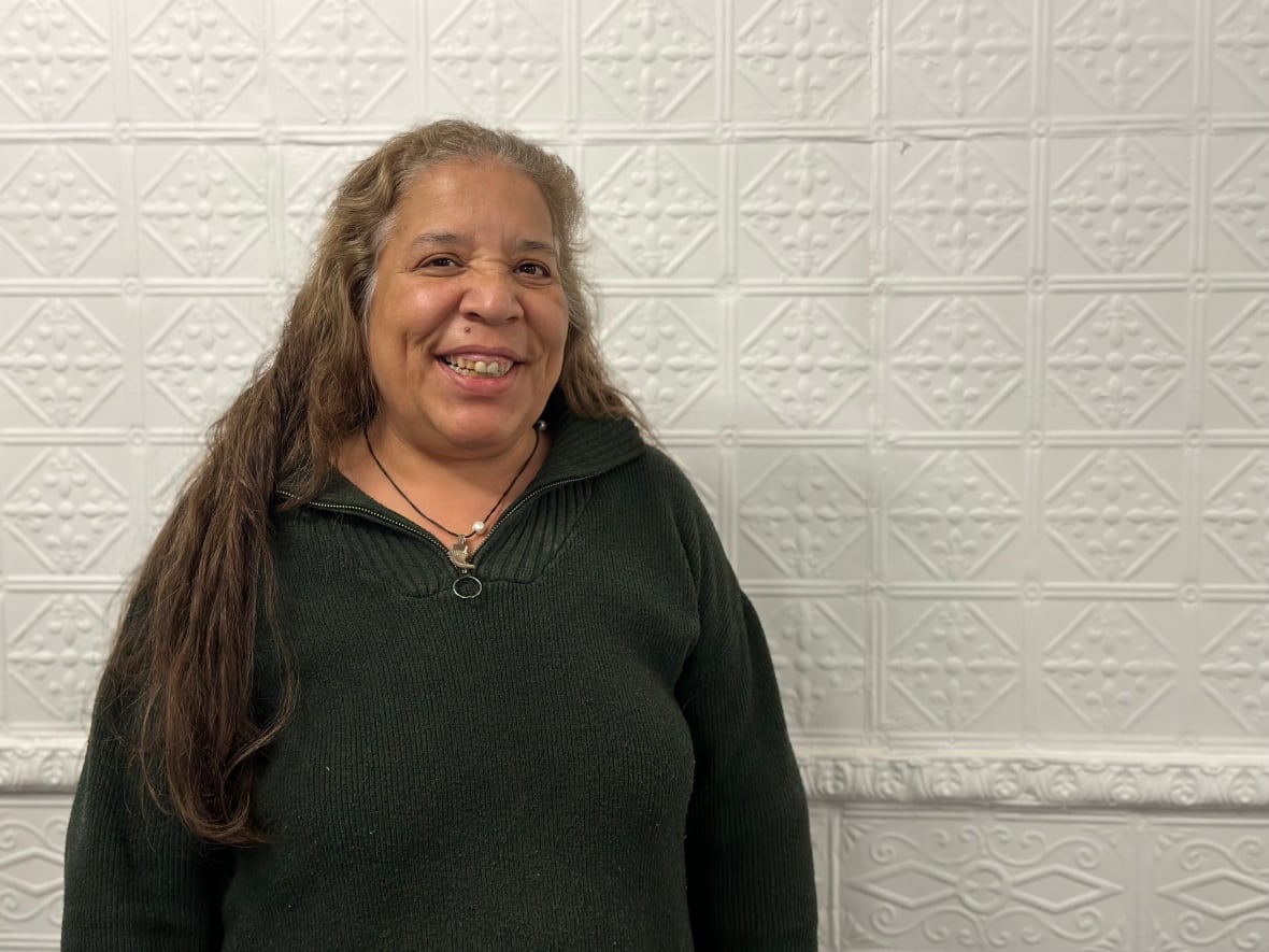 A woman with long brown hair and a green sweater smiles at the camera.