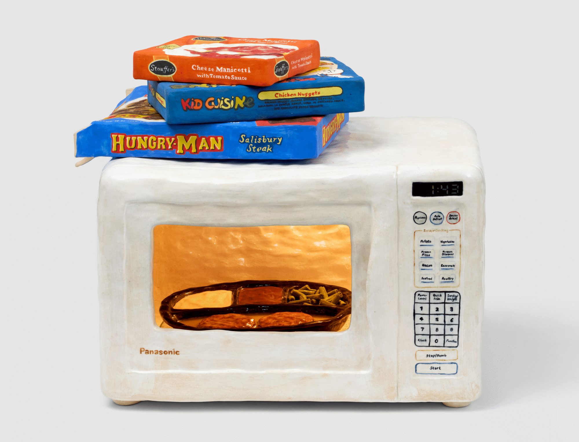 a ceramic sculpture of a tv dinner platter rotating inside of a lit microwave. three boxes of tv dinners sit above the microwave, including Stouffer's, Kid Cuisine, and Hungry-Man.
