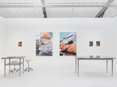 View of an art fair booth showing photorealist paintingsof hands at sleek objects. 