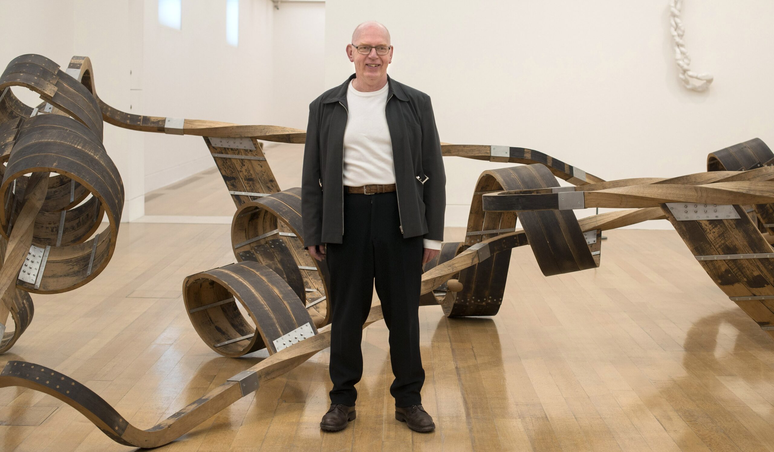 Richard Deacon standing with his sculpture at the Tate Britain.