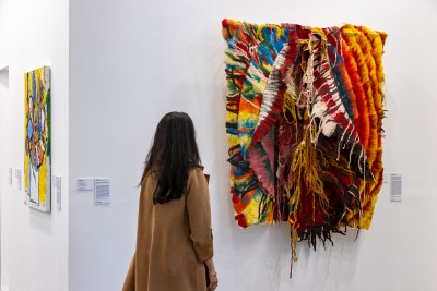 A woman looks at a textile artwork that is made of various textiles and yarns sewn together. 