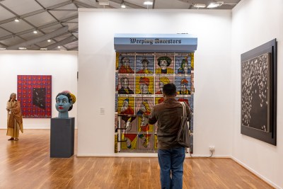 A man stands in front of an artwork in an art fair booth. 