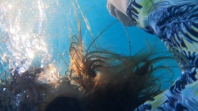A film still of a woman's head as she is submerged in blue water. 