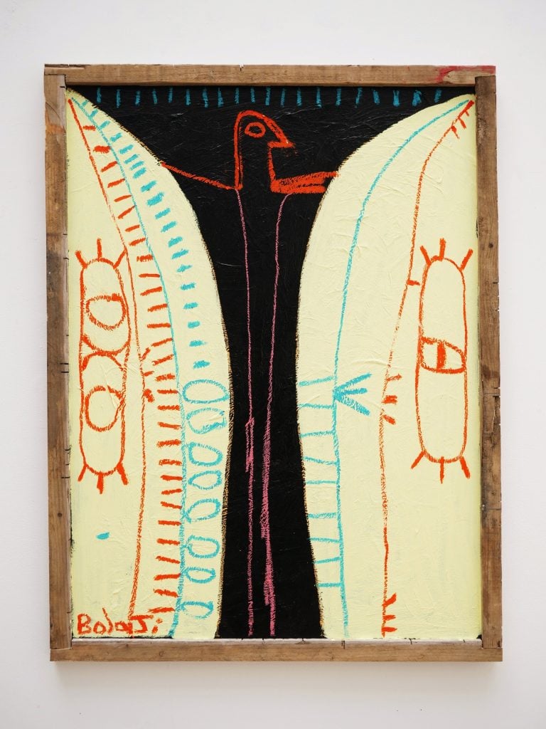 A painting titled La Manifestation 01 by Adebayo Bolaji, exhibited at Galerie Kremers. The artwork features bold, expressive lines and a mix of abstract and figurative elements. A central black figure with red facial features and outstretched arms appears to emerge from or be framed by two large, pale yellow shapes with intricate patterns in blue and orange. The piece is enclosed in a rustic wooden frame, emphasizing its raw, spontaneous aesthetic, reminiscent of neo-expressionism and African-inspired symbolism. The artist's signature,