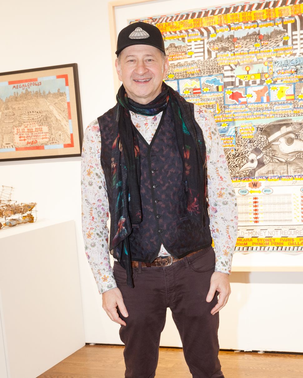 A man with a hat, gilet and white shirt sorrounded by art. 