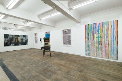 View of an art gallery with two paintings on walls and a mixed-media sculpture in the center. 