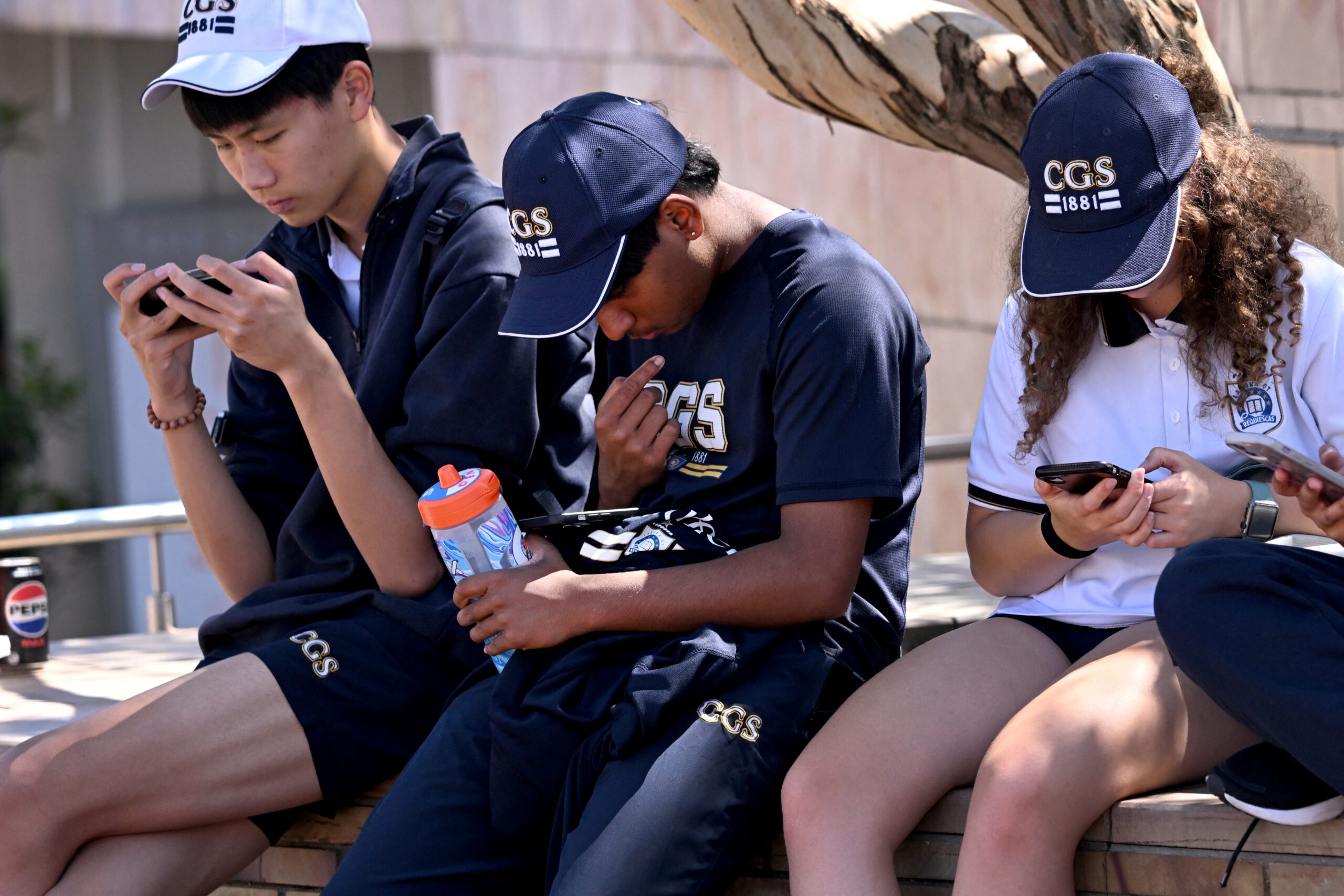 Three students sitting outdoors looking at their phones.