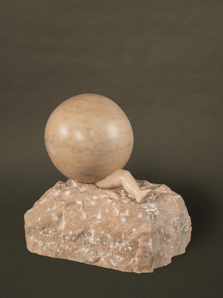 A photo of a pink marble sculpture sitting against a dark gray backdrop. It shows a smooth sphere sitting on a roughly hewn chunk of marble, with a tiny, chubby baby leg seemingly crushed by the sphere. The phrase