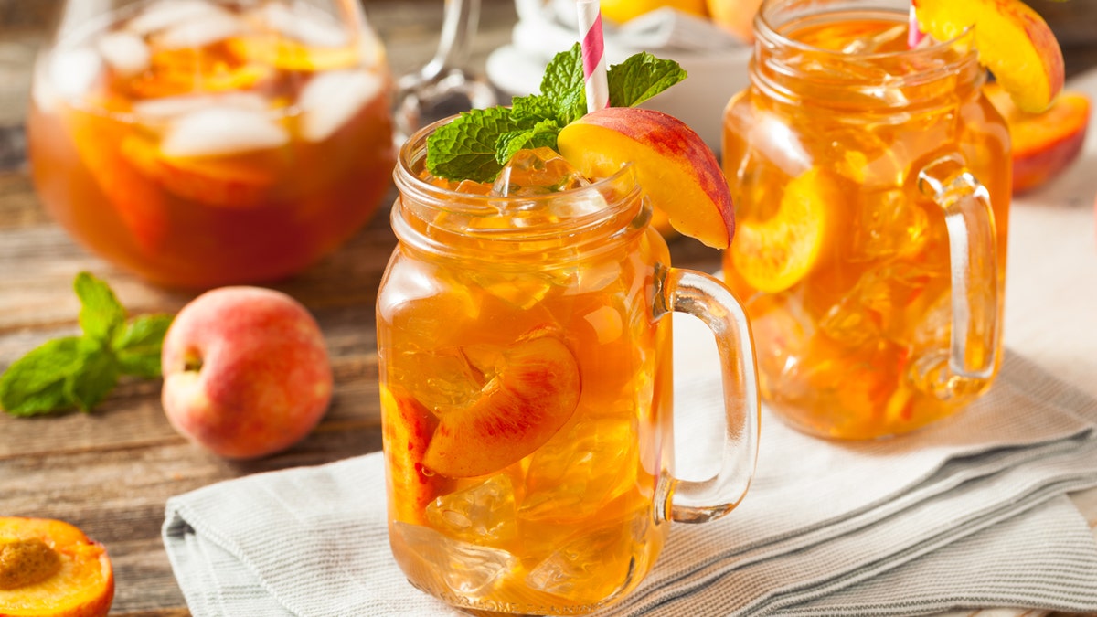 Two glass mason jars of peach-flavored iced tea.