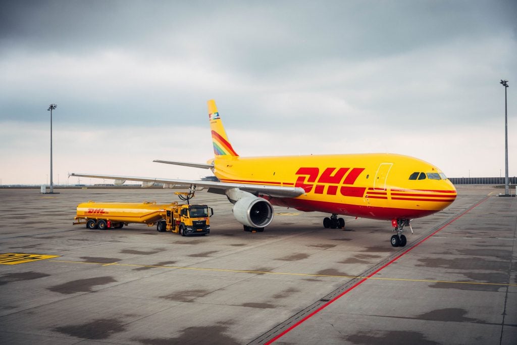 a large yellow DHL shipping plane stands on a tarmac