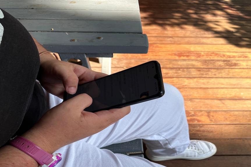A young woman in white pants scrolls on her phone.