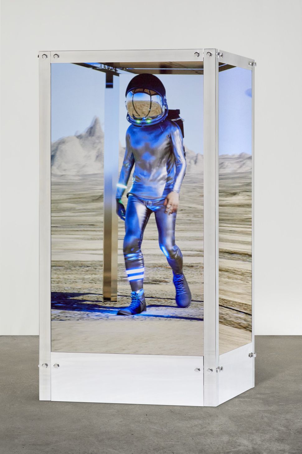 Digital and physical hybrid sculpture by Beeple featuring a rotating, futuristic figure walking endlessly through shifting virtual landscapes inside a transparent box.