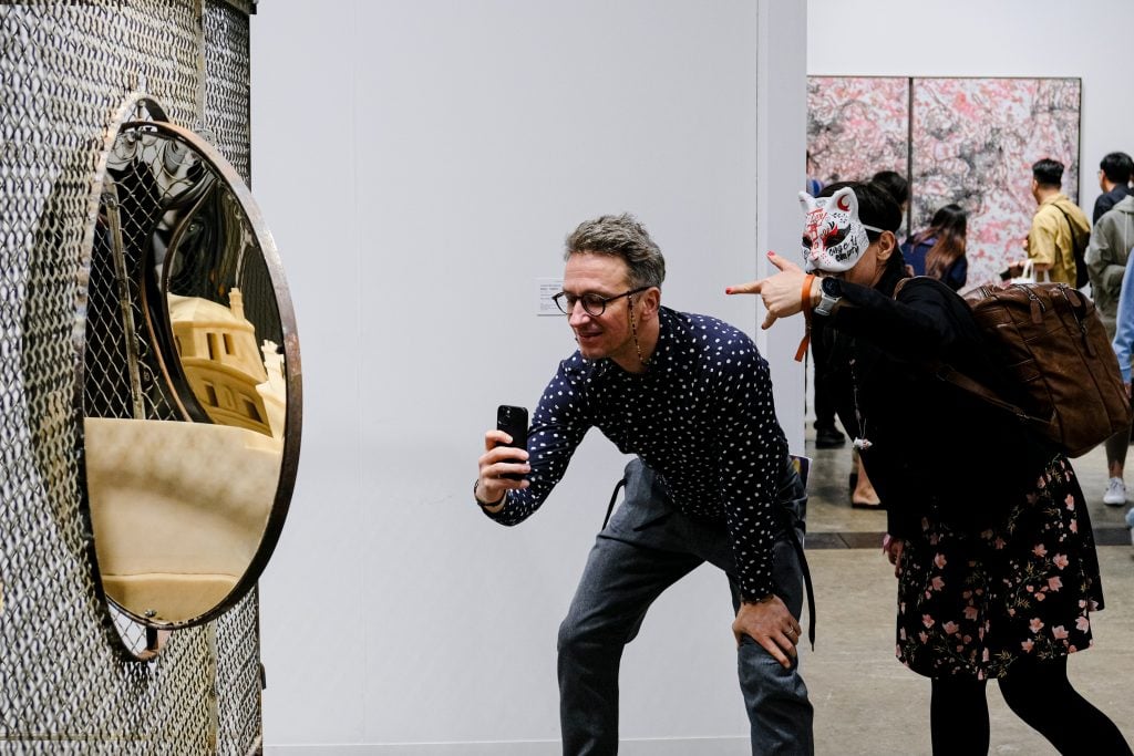 Visitors interact with a reflective mixed-media artwork at Expo Chicago 2025, highlighting playful audience engagement and immersive contemporary art experiences.